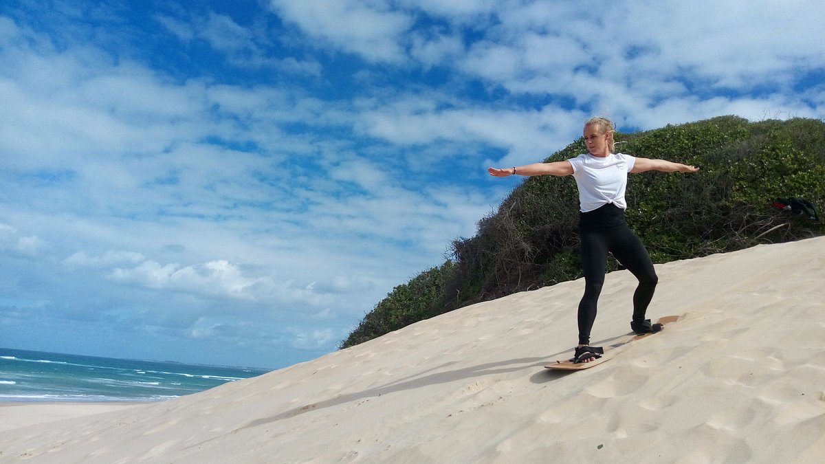 Sandboarding down golden coastal dunes near Jeffreys Bay with ocean views